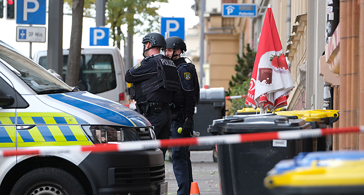 Två poliser står bredvid en polisbuss. Området är avspärrat med röd och vit tejp.