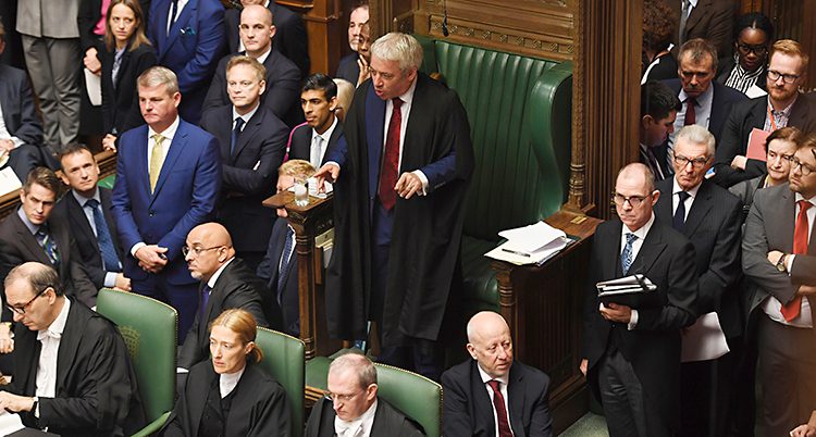 En bild från riksdagen i Storbritannien. Folk sitter i gröna bänkar. En man med grått hår står upp och pratar.