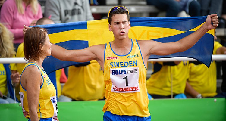 En man håller upp en stor svensk flagga över axlarna. Han har solglasögon i pannan och ett gult linne som det står Sweden på.