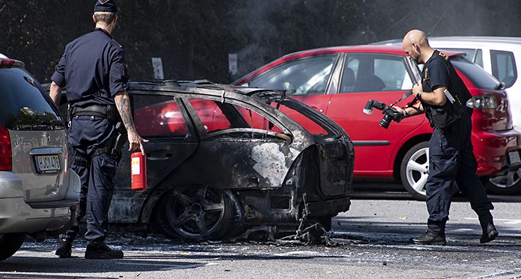 Två poliser tittar på en bränd bil.