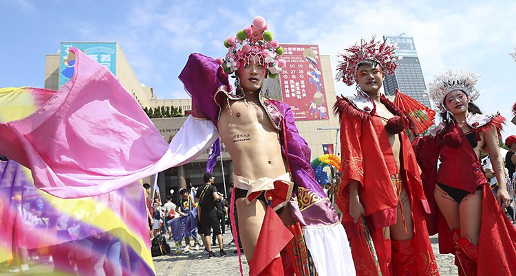 Tre personer är utklädda i prideparaden i Taiwan. De har kronor på huvudet och röda sidenkläder på kroppen.