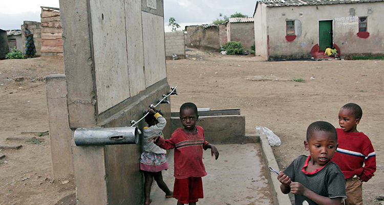 Barn i Zambia leker utomhus. Husen runt dem är slitna.