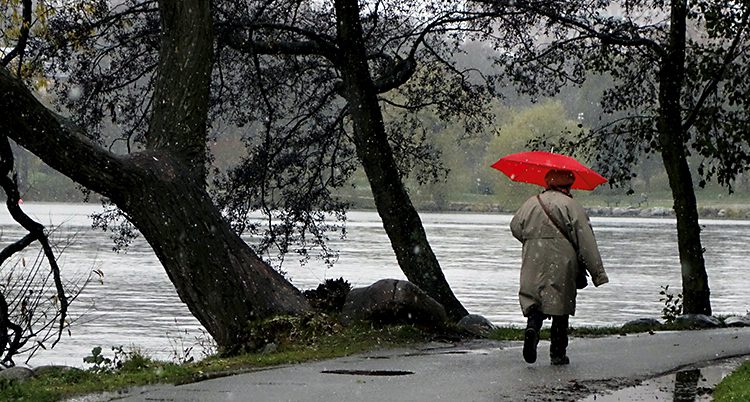 En kvinna promenerar. Hon har ett rött paraply i handen.