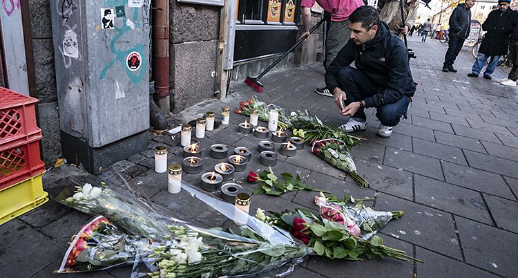 En man sitter på hus på trottoaren. Framför honom finns blommor och ljus.