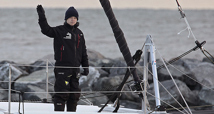 Greta Thunberg är just nu på en segelbåt. Den ska ta henne till ett möte om klimatet i Spanien. På bilden står hon upp i båten och vinkar.