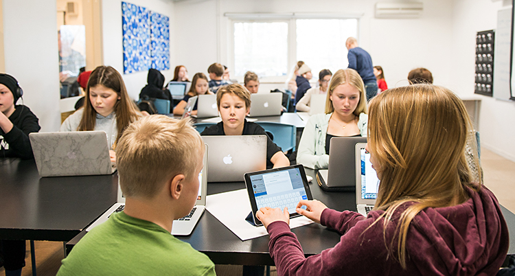 Elever sitter med egna datorer i ett klassrum.