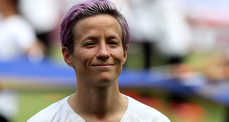 Fotbollsspelaren Megan Rapinoe innan en match. Hon tittar in i kameran och ler. Hon har färgat sitt hår lila.