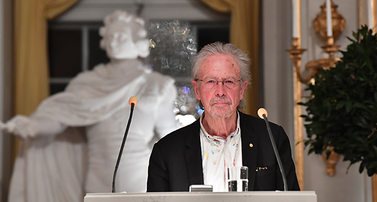 Han står framför en vit staty och talar i mikrofon