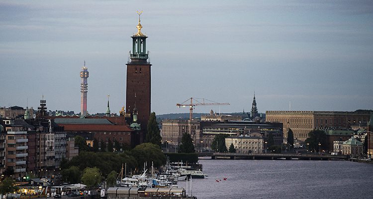 Flera kända hus i Stockholm syns på bilden. Båtar och vatten syns. Det är skymning.