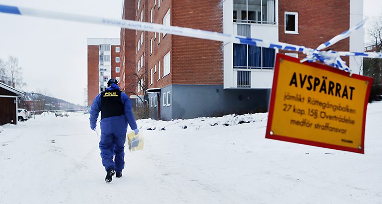 En polis går på vägen. Några höghus syns i bakgrunden. Området har spärrats av av vit och blå polistejp.