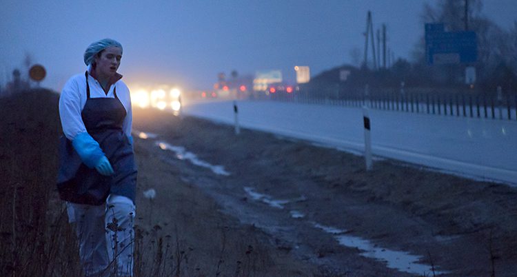 En kvinna går i vita jobbkläder längs en mörk väg