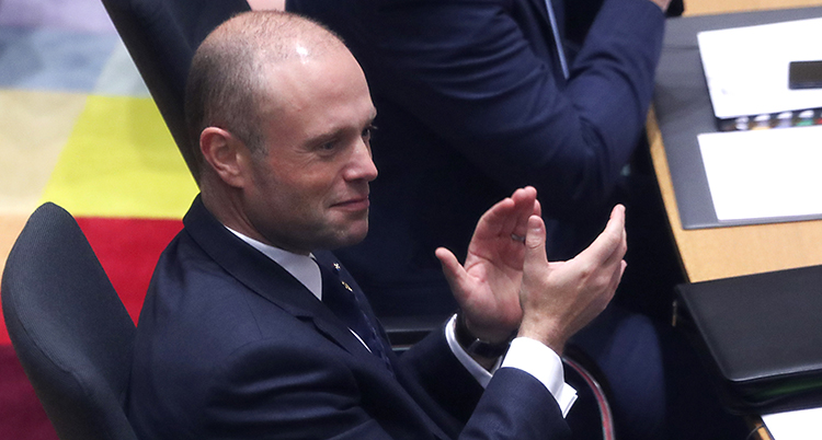 Maltas ledare Joseph Muscat sitter på ett möte i EU. Han applåderar med händerna. Han har rakat huvud och kostym.