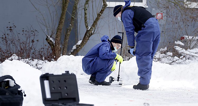 Bilden är tagen utomhus i ett bostadsområde i Sundsvall. Det är snö på marken. Två tekniker från polisen arbetar med att hitta spår efter ett mord.