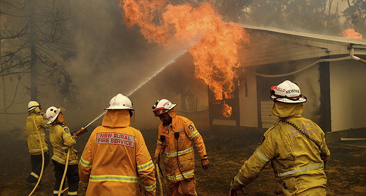 Det brinner i ett hus. Lågorna slår ut genom ett fönster. Brandmän sprutar vatten.