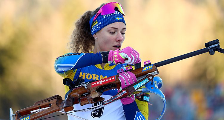 Skidskytten Hanna Öberg gör sig redo för att skjuta. Hon har på sig Sveriges tävlingskläder. Hon gör något med sitt gevär.