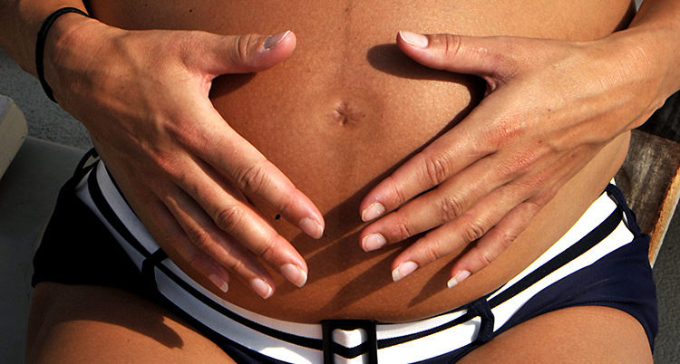 En gravid kvinnas mage. Båda kvinnans händer vilar på magen.