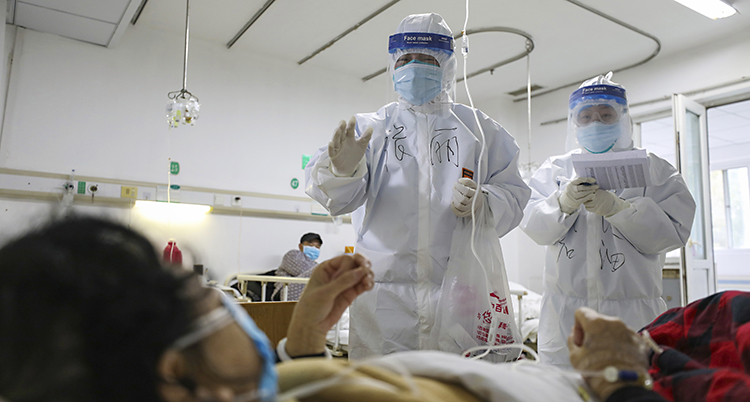 Två som jobbar på ett sjukhus i Kina. De tar hand om en patient som har fått den nya smittan. De som jobbar har skyddande vita kläder på sig och masker för ansiktet.