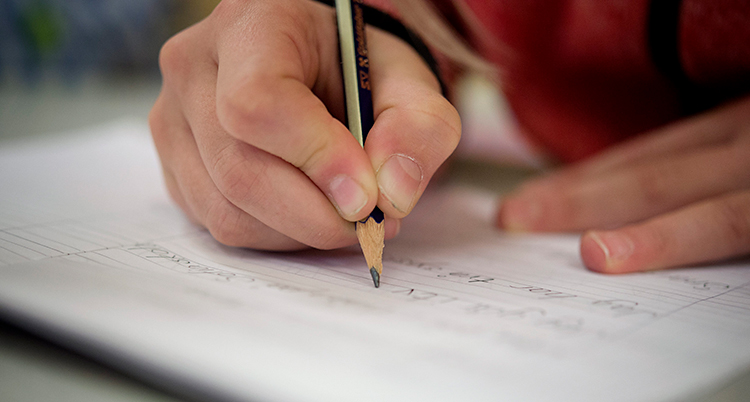 Bilder visar en elev som skriver i skolan. Man ser bara händerna på eleven.