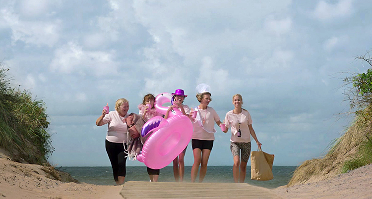 Fyra personer går på en strand med en stor rosa leksaksflamingo
