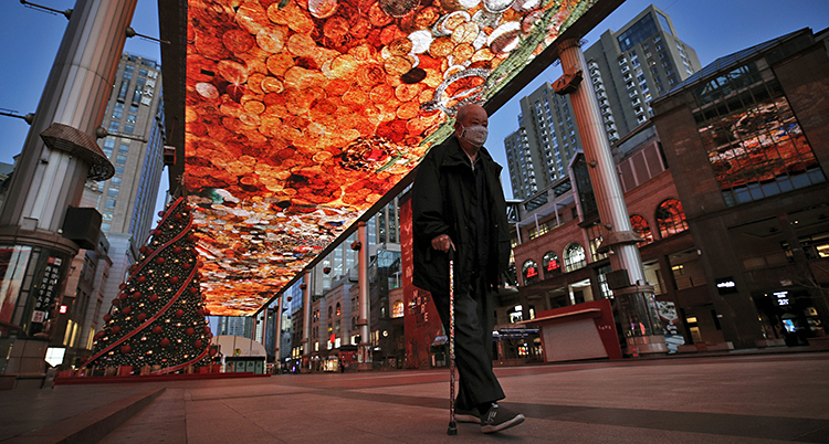 En äldre man med käpp fotad underifrån. Han går på en smal shopping gata i Beijing. Han är helt ensam. Ovanför honom är himlen mellan husen smyckade med röda dekorationer.