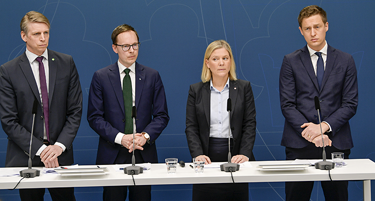 Fyra politiker i mörka kostymer med mikrofoner framfor sig.