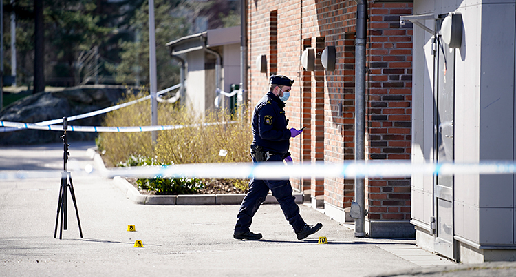 Bilden är tagen utomhus vid en skola. Poliserna har satt upp ett avspärrningsband. Bakom bandet går en polis med ett munskydd.