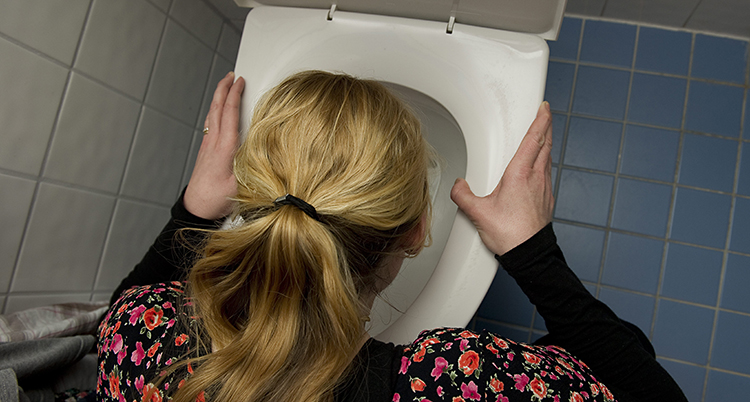En kvinna kräks ner i en toalett.