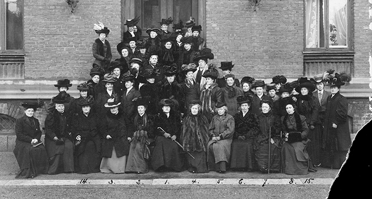 Ett gammal svartvitt foto med många kvinnor samlade utanför ett hus