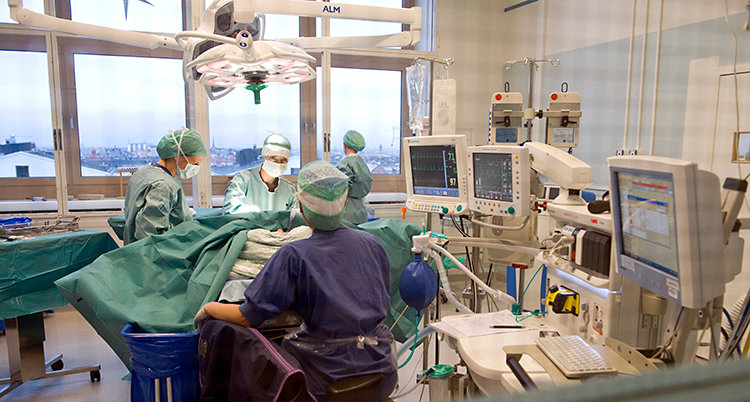 Bilden är från ett rum på ett sjukhus. Läkare och sjuksköterskor gör en operation. Patienten är dold bakom ett skynke.