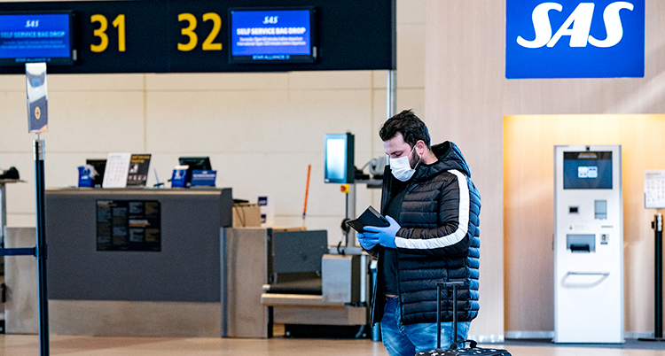 En man med munskydd står vid SAS disk på Arlanda. Han tittar ner i en bok