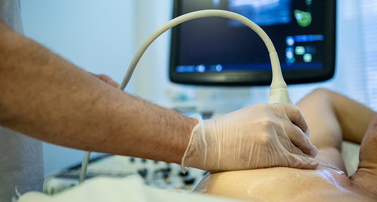 en plastklädd hand håller i ett ultraljud som trycks mot en del av en kvinnas kropp.