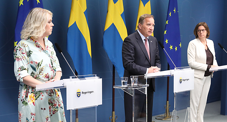 Tre politiker står på en scen. De pratar i mikrofoner. I bakgrunden finns svenska flaggor och EUs flagga.