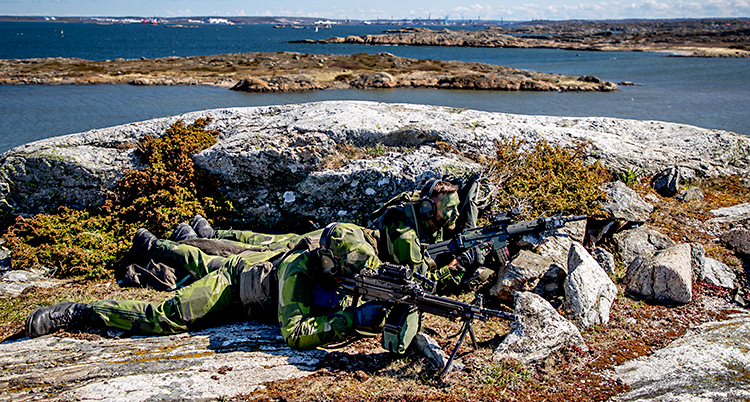 Bilden är från skärgården i Göteborg. Två män ligger på en klippa. De har gröna kläder och vapen.