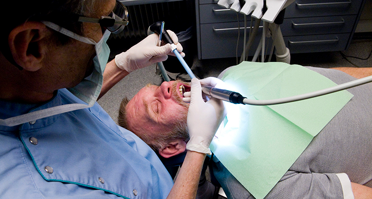 En tandläkare undersöker en man i munnen med ett verktyg.