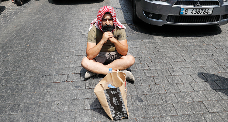 En man sitter ner på gatan med benen i kors. Han har shorts på sig och ett slags turban på huvudet.