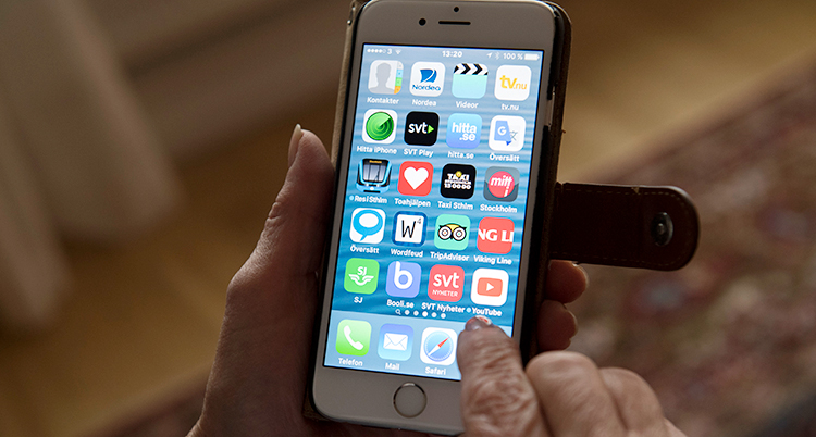 En hand håller i en mobiltelefon. På telefonen syns många appar.