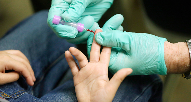 Sjukvårdspersonal med ljusgröna handskar tar ett blodprov på ett barn.