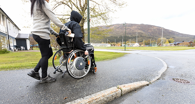en kvinna kör en man i en rullstol på en gata.