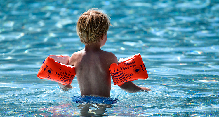 Ett barn står i en pool. Ryggen syns.