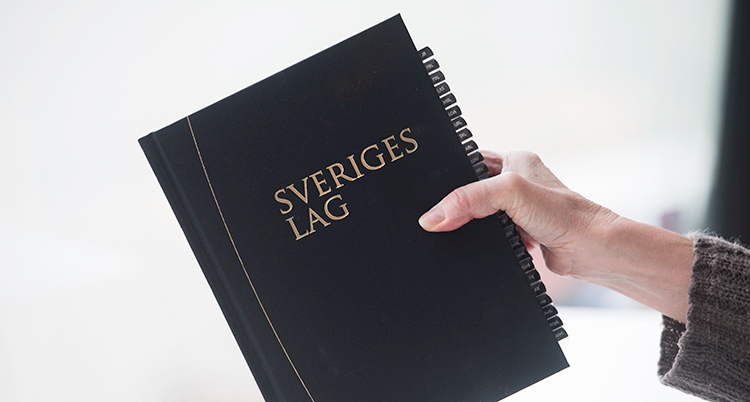 En hand håller upp lagboken som är svart. Där står Sverige lag.