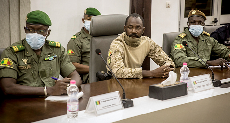 Tre militärer i Mali sitter vid ett bord. Två av dem har på sig munskydd och soldatuniformer.