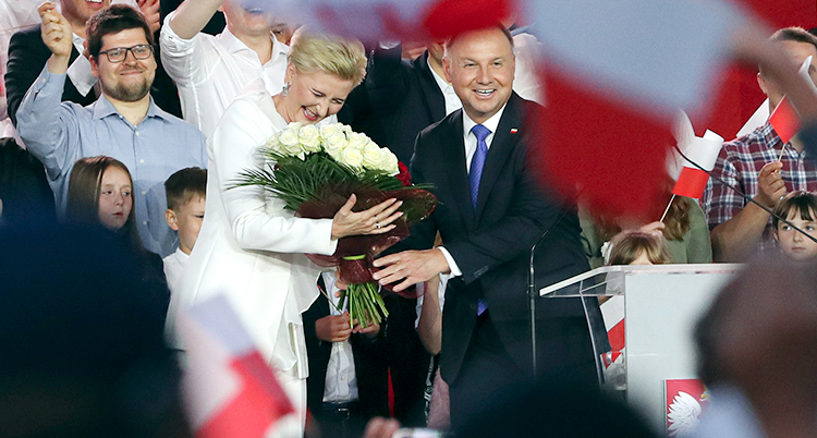 Andrzej Duda och hans fru får blommor av folk som stödjer Duda. De ser glada ut och människor i bakgrunden viftar med flaggor. Bilden är från valdagen den 12 juli.