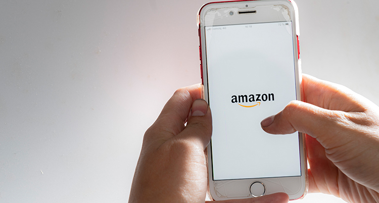 En bild på ett par händer som håller i en mobil. På mobilen syns Amazons logga.