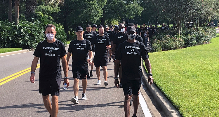 En lång rad med med i svarta tröjor går i en park. På tröjorna stor det Everyone vs. Racism.