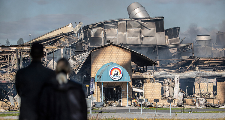 Två personer står framför fabriken som är förstörd av branden.