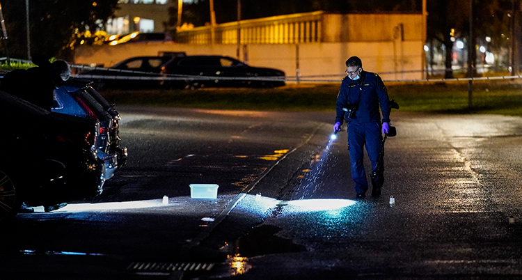 En kvällsbild på poliser med ficklampa som lyser på en brottsplats.