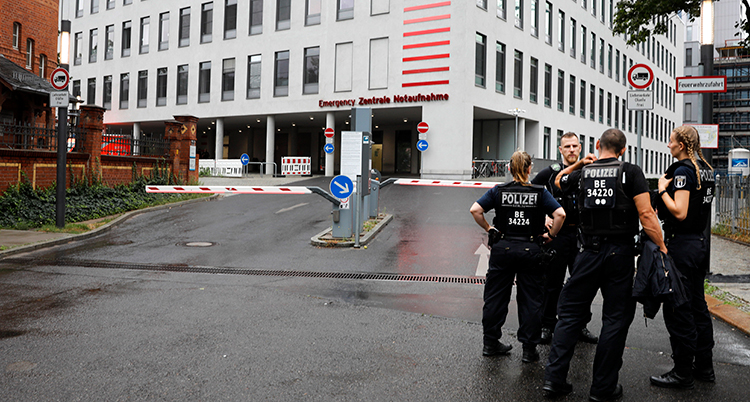 Fyra poliser står vid två bommar över en väg. Bakom dem är ett stort grått hus.