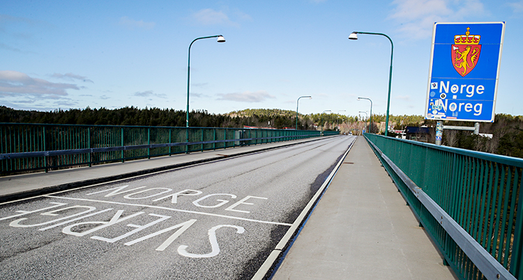 En bilväg på en bro. Mitt på bron står det Sverige. På andra sidan av ett streck står det Norge. På bron finns också en skylt där det står Norge.