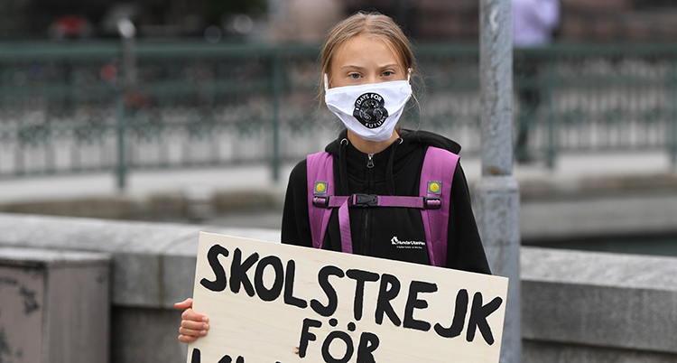 Hon har munskydd på sig och en skylt i händerna. På den står det skolstrejk för klimatet.