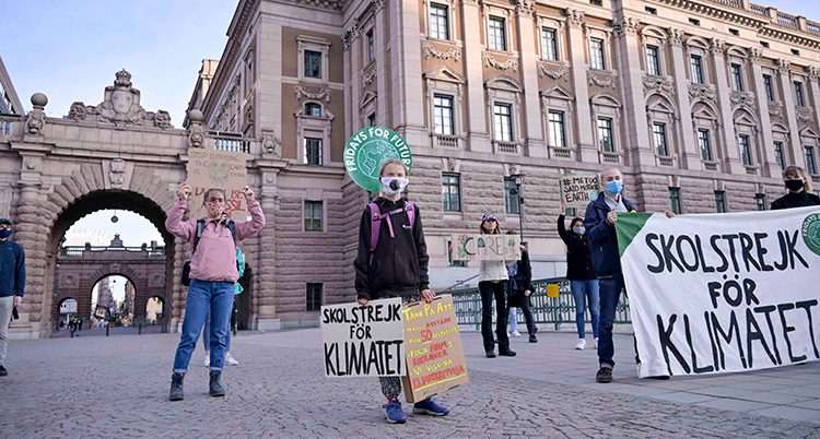 Greta Thunberg och några andra unga framför riksdagshuset. De har masker för munnen.